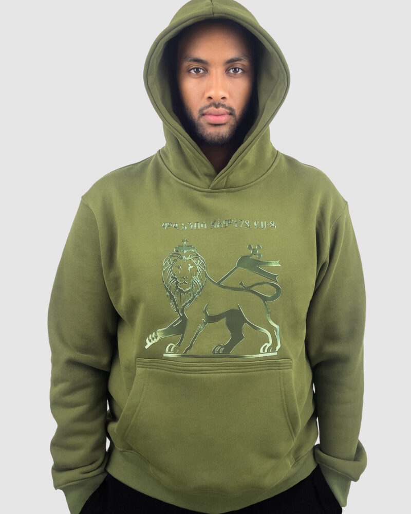 Front view of a man wearing an olive-green heavyweight hoodie with an HF-embossed glossy PU Lion of Judah graphic and Amharic lettering on the chest.
