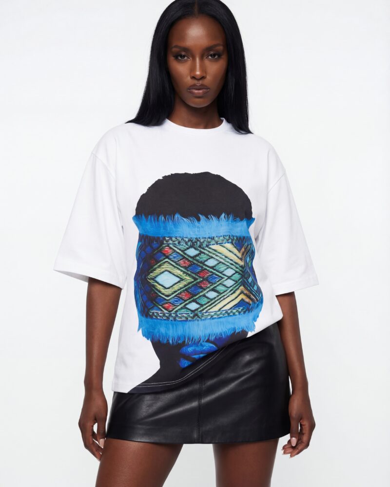 Front view of a woman wearing a white oversized boxy-fit T-shirt featuring a large graphic of an Ethiopian woman’s silhouette with a blue Tilet-inspired woven textile band across her eyes.