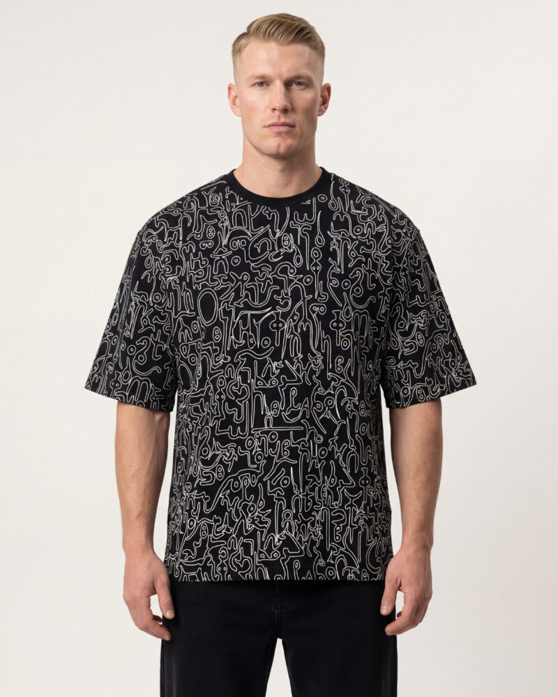 Front view of a man wearing a black oversized boxy-fit heavyweight T-shirt with an all-over abstract white line-art print inspired by playful Ge’ez-script sketches.